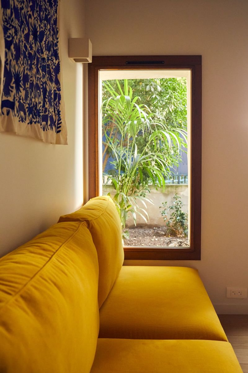 Banquette jaune devant une fenêtre ouverte sur le jardin