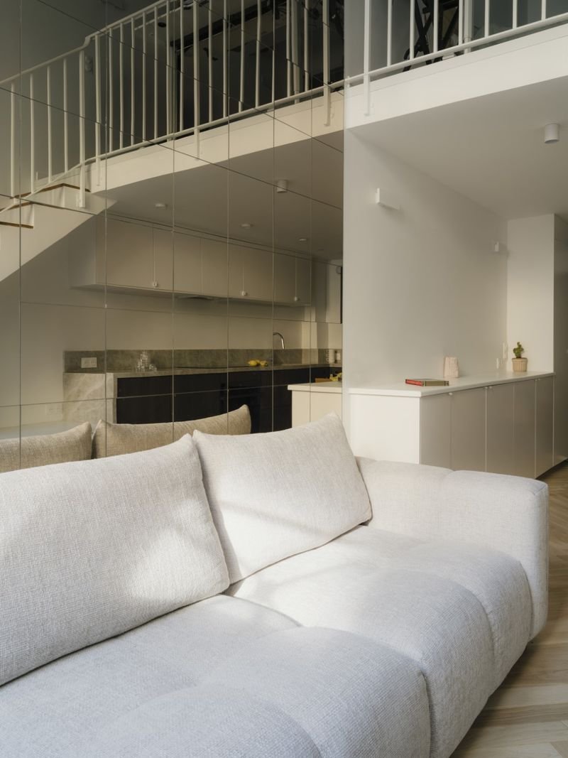 Canapé clair du séjour, cuisine reflétée dans le mur de miroirs