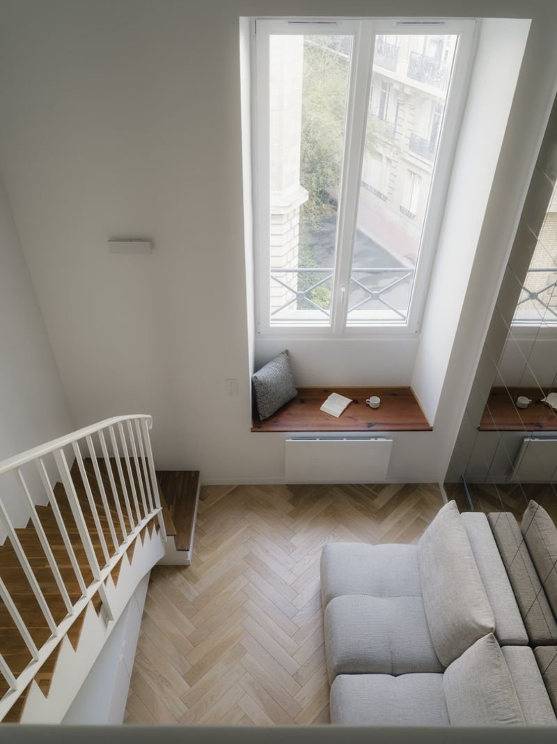 Séjour vu de la mezzanine : canapé, banquette sous la fenêtre et parquet à bâtons rompus