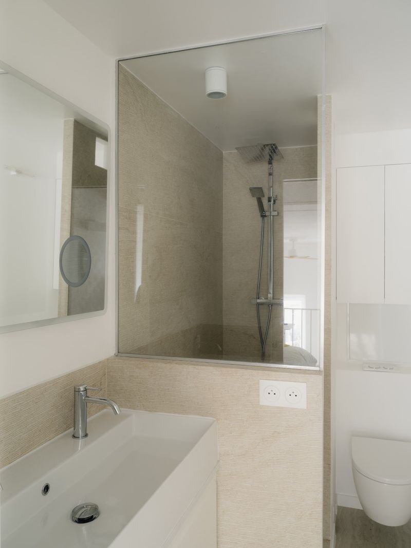 Salle d’eau : vasque blanche et douche derrière une paroi vitrée