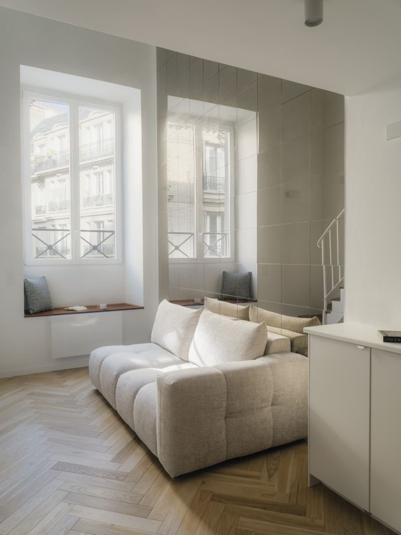 Canapé clair devant un mur de miroirs, banquette en bois sous la fenêtre