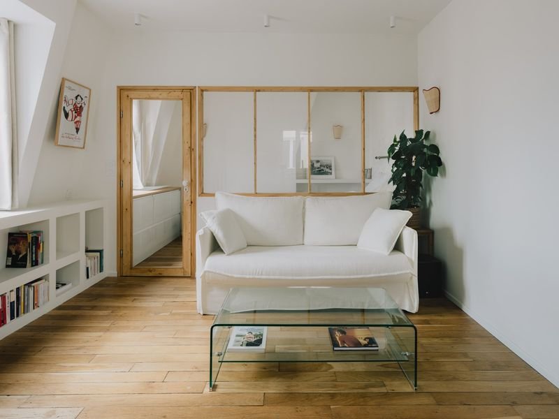 Séjour de l’appartement Tardieu à Paris 18e : canapé blanc devant la verrière en bois de la chambre